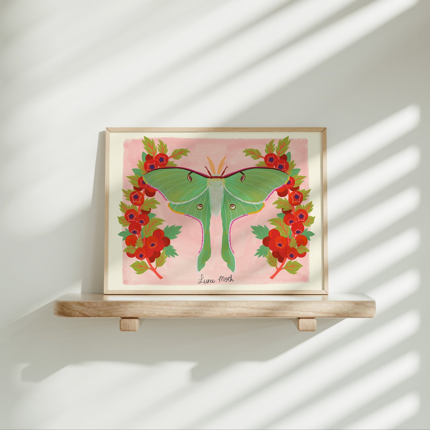 Framed artwork of a green butterfly with red flowers on a pink background, placed on a wooden shelf.