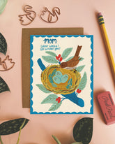 Greeting card with bird and nest illustration on a pink background with decorative elements.
