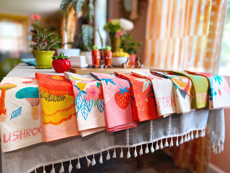 bright, colorful hand made dish towels hanging on a kitchen table.